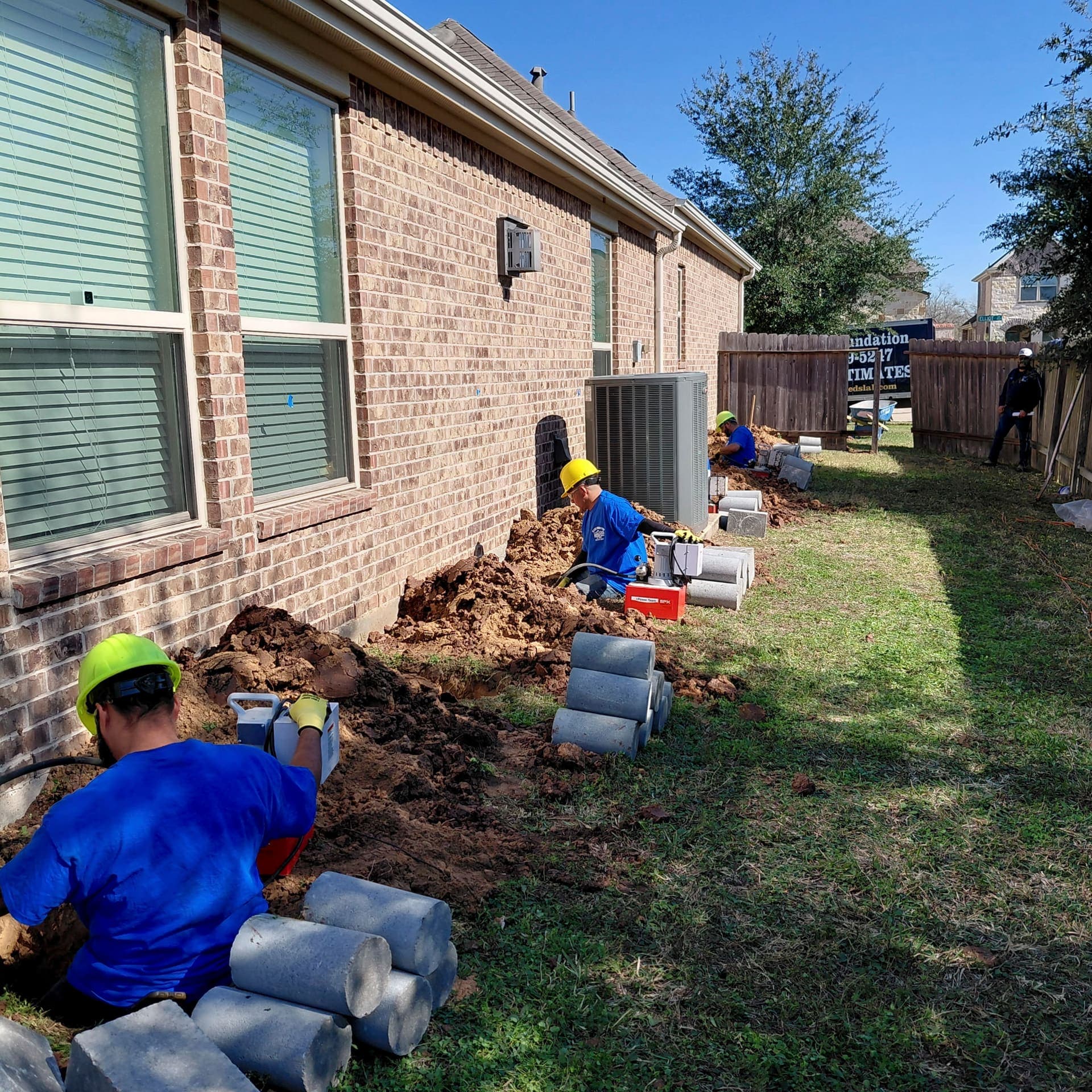 Light brick home with Allied workers in yellow helmets and blue shirts working at the exterior wall