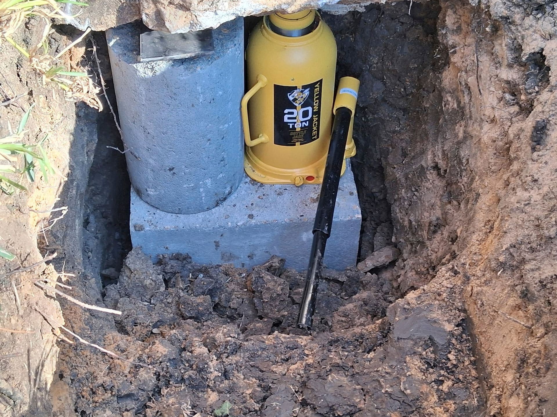 Yellow hydraulic jack on a block beside a concrete cylinder inside the excavation