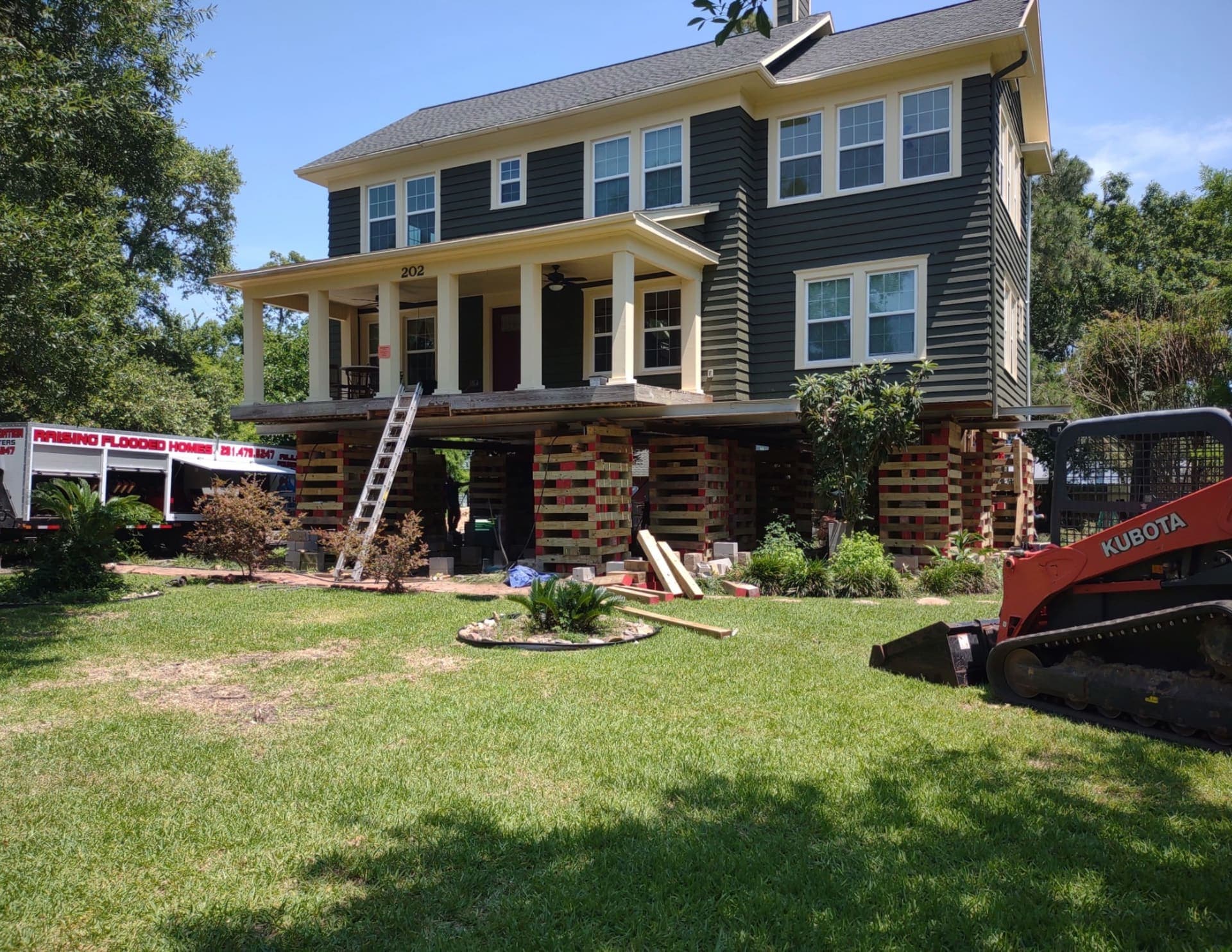 Green and yellow home elevated and resting on cribbing during a house lifting project