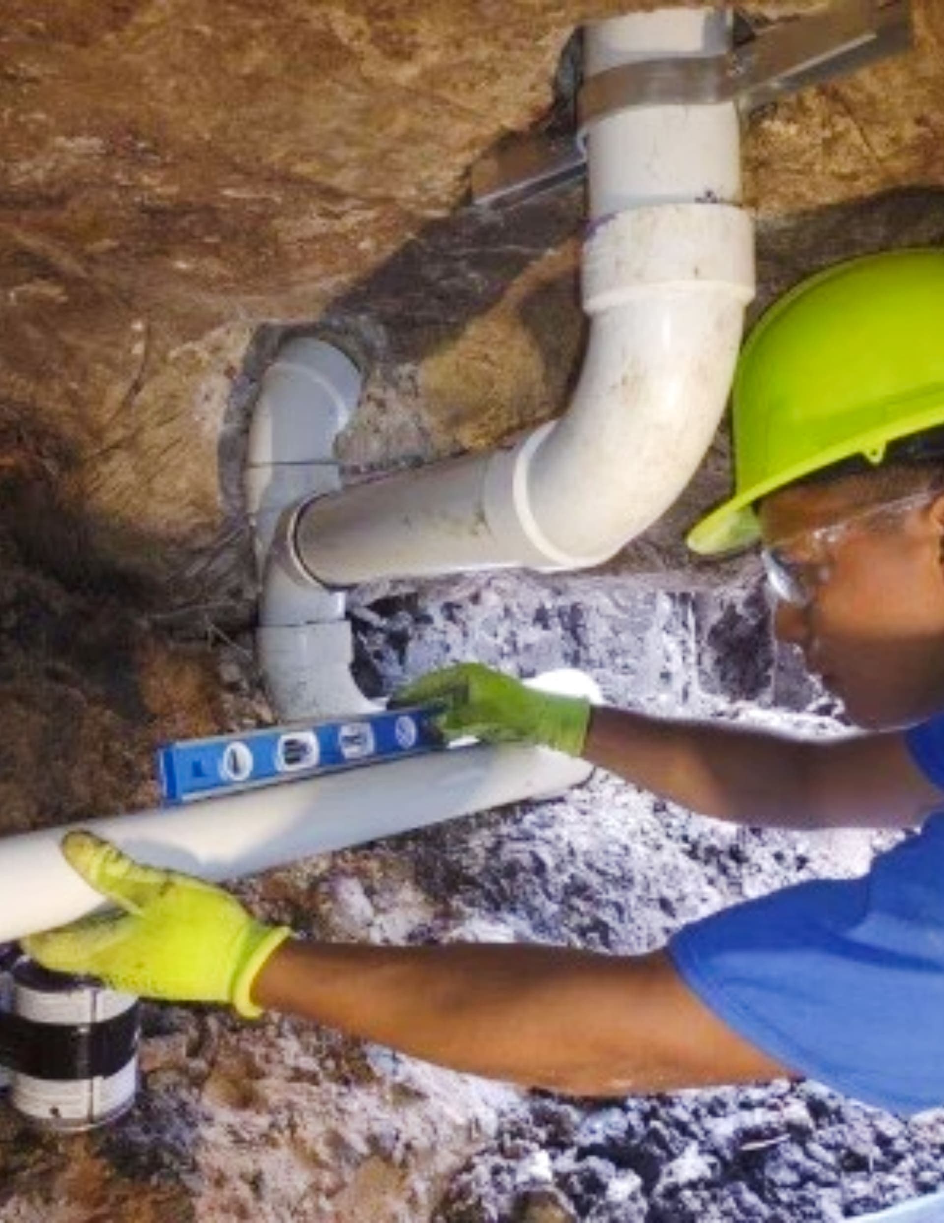 Allied Foundation worker in a yellow helmet and blue shirt checking PVC pipe with a blue level inside a tunnel