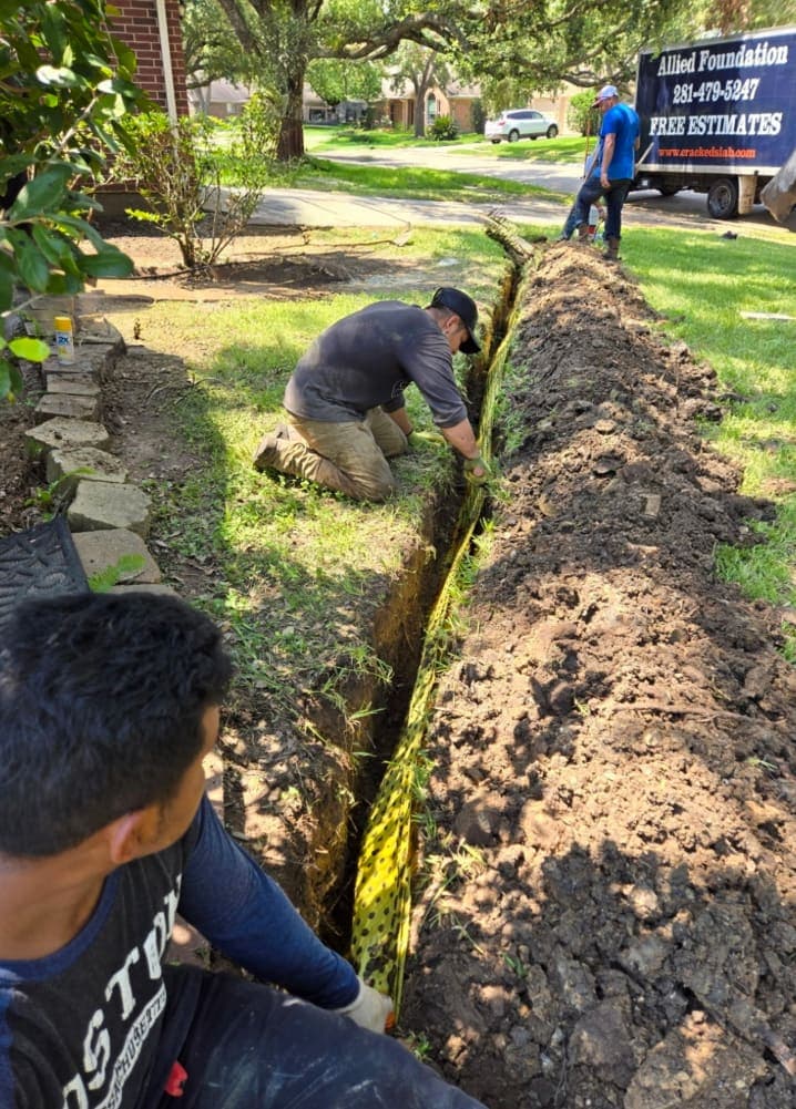 Three Allied Foundation workers installing yellow BioBarrier® root barrier fabric in a trench beside a lawn
