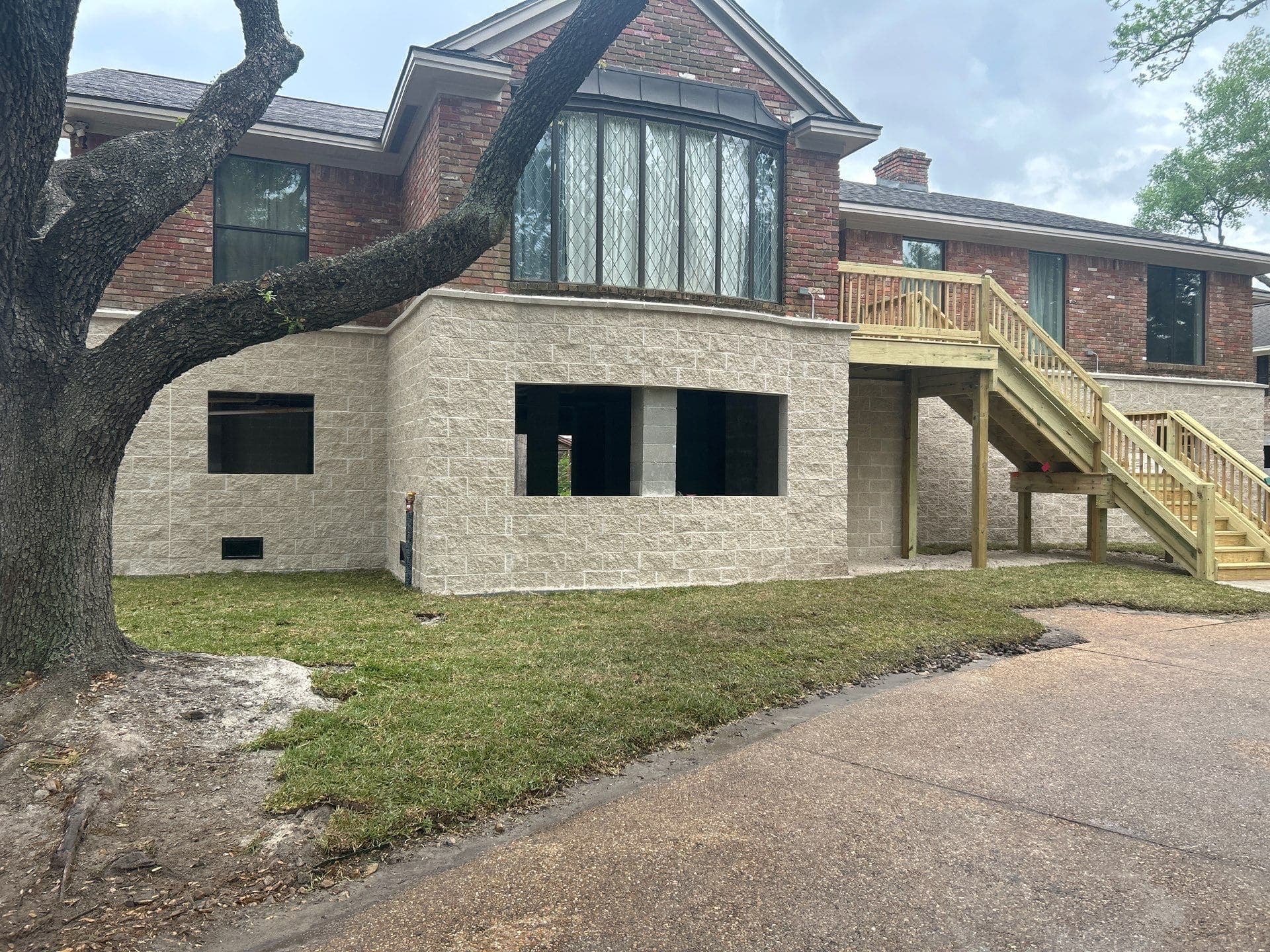 The same red brick house raised with a skirt wall, with the leafless tree at left