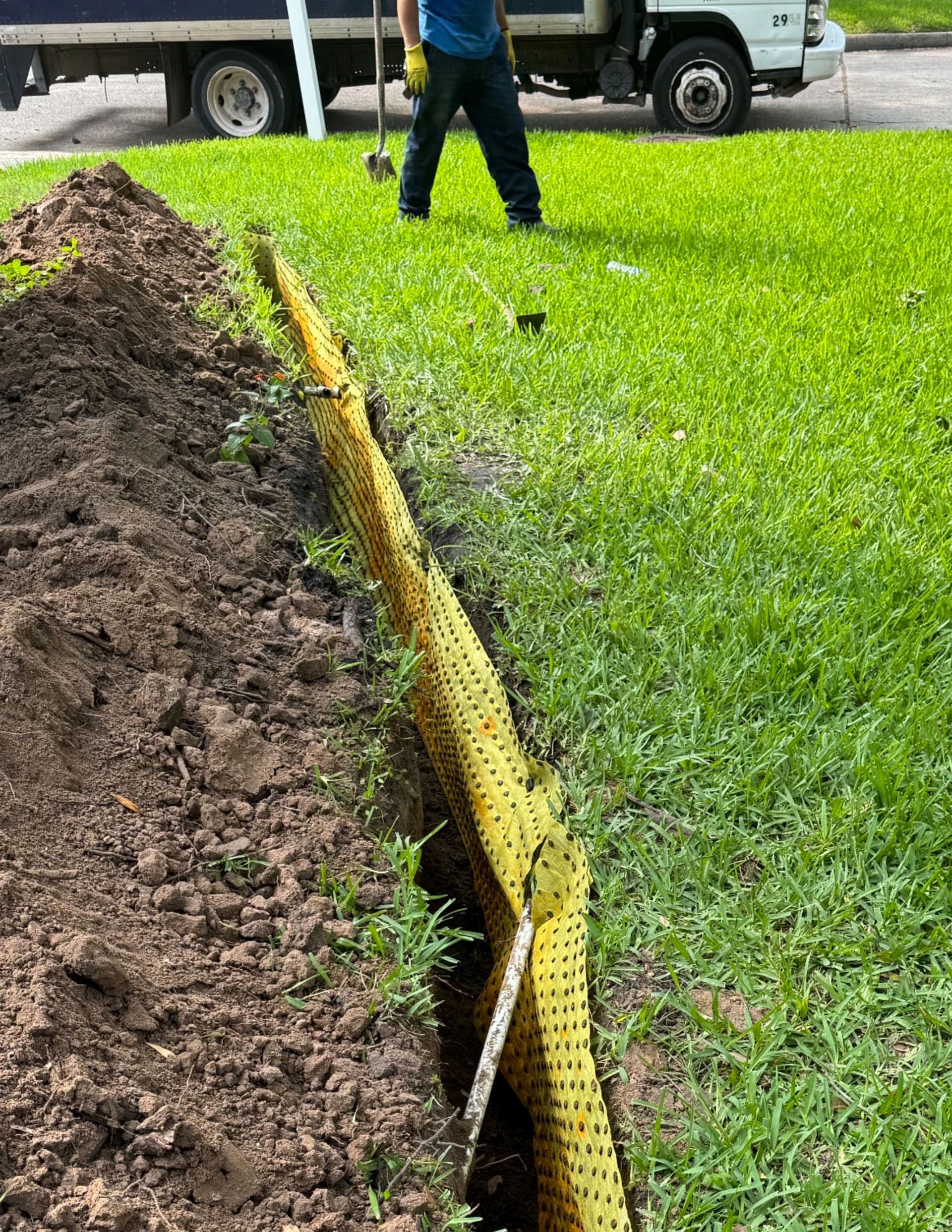 Yellow BioBarrier® installed in the trench with one worker and truck wheels in the background