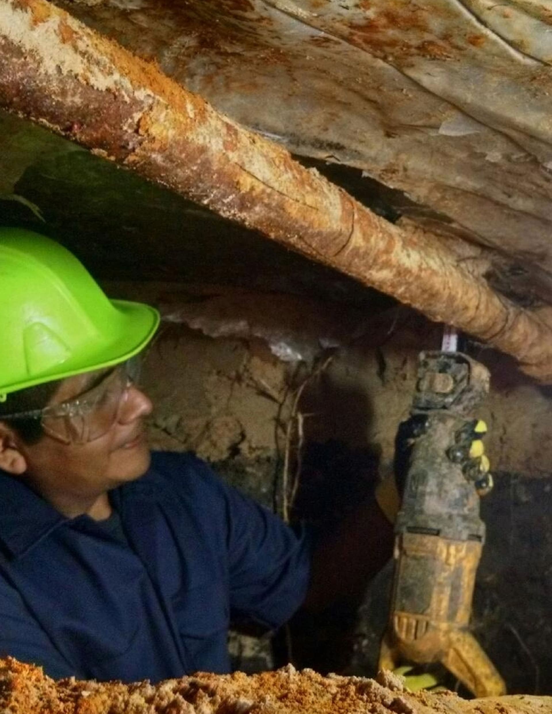 Allied worker in a yellow helmet cutting old cast iron pipe with a reciprocating saw