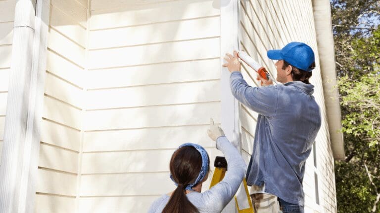 a man and woman painting the outside of a house