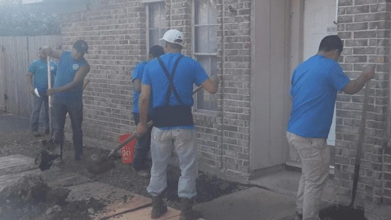 four men in blue shirts are shoveling the sidewalk