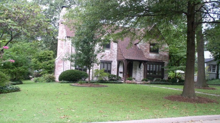 a brick house surrounded by trees and bushes